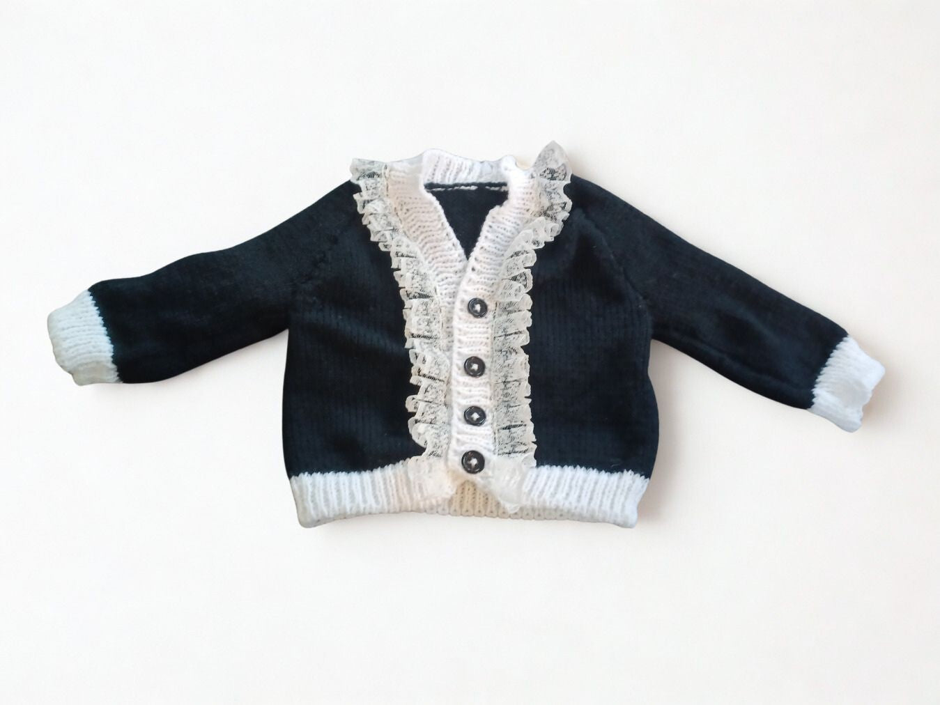 Long sleeved black cardigan with white trim and lace around the neck edge.