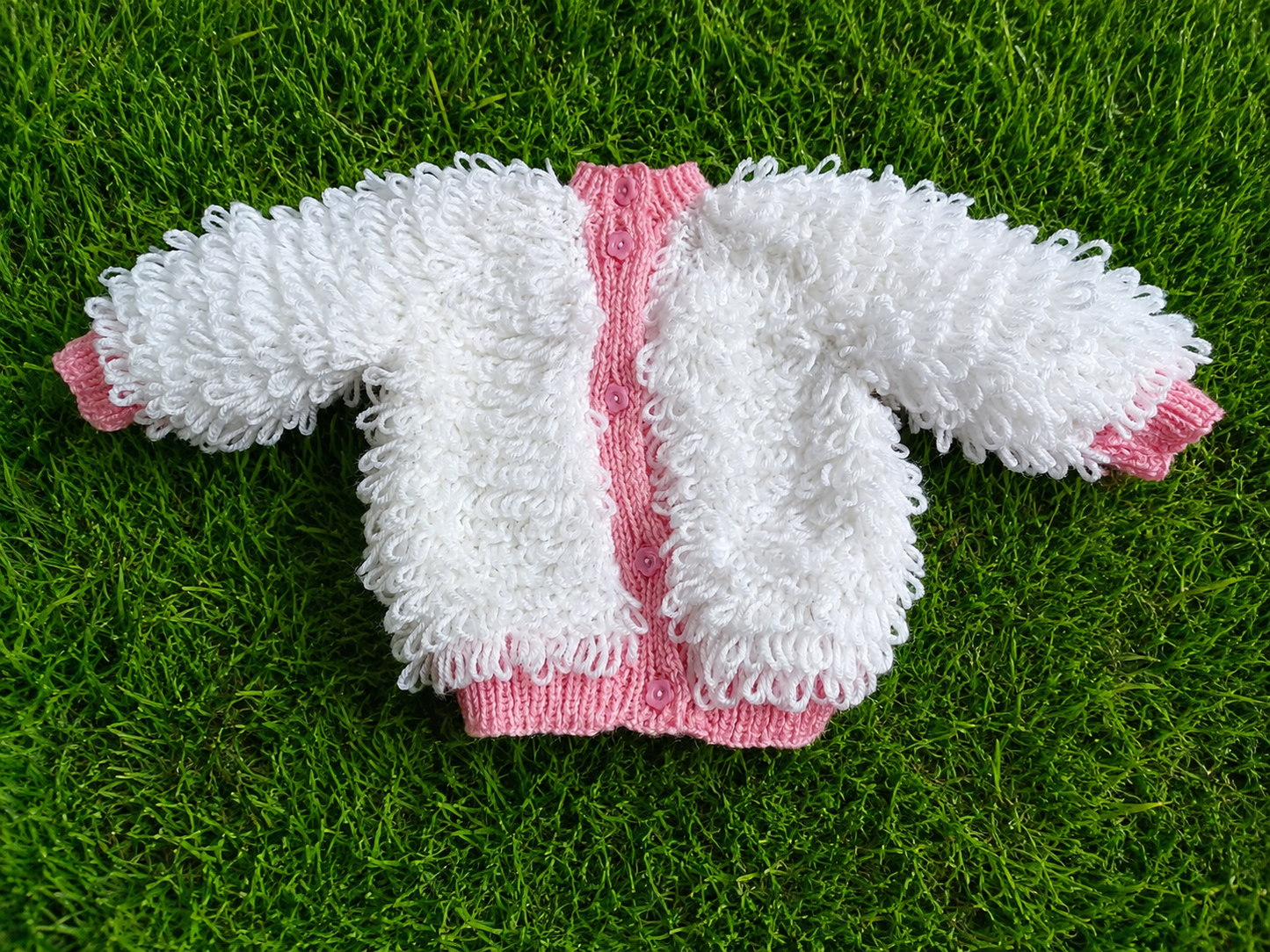 A lovely white loopy-knit cardigan with charming pink edging, soft texture, and delicate pink buttons for a beautifully feminine finish.